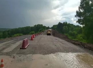 Тяжелая дорожно-строительная спецтехника, включая экскаватор и грунтовый каток, восстанавливает разрушенный оползнем участок междугородней трассы.